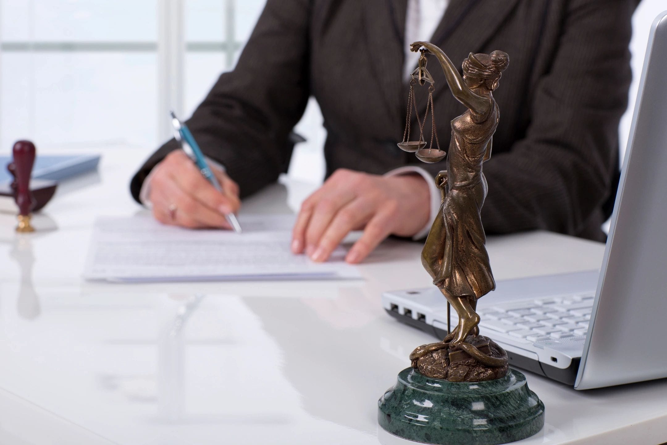 A person writing on paper next to a statue of lady justice.